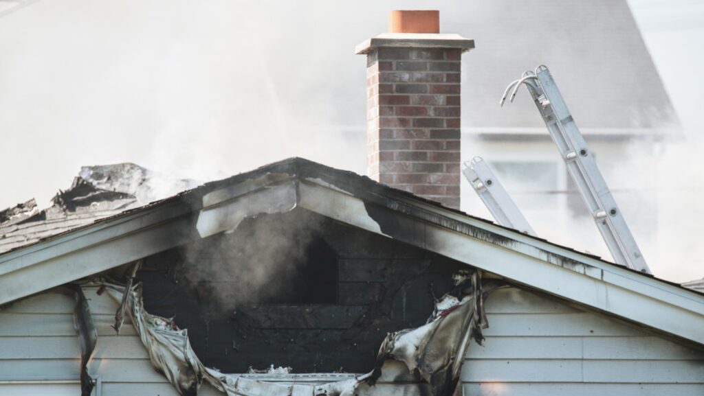 The roof of a house with a large black hole from where fire has damaged it.