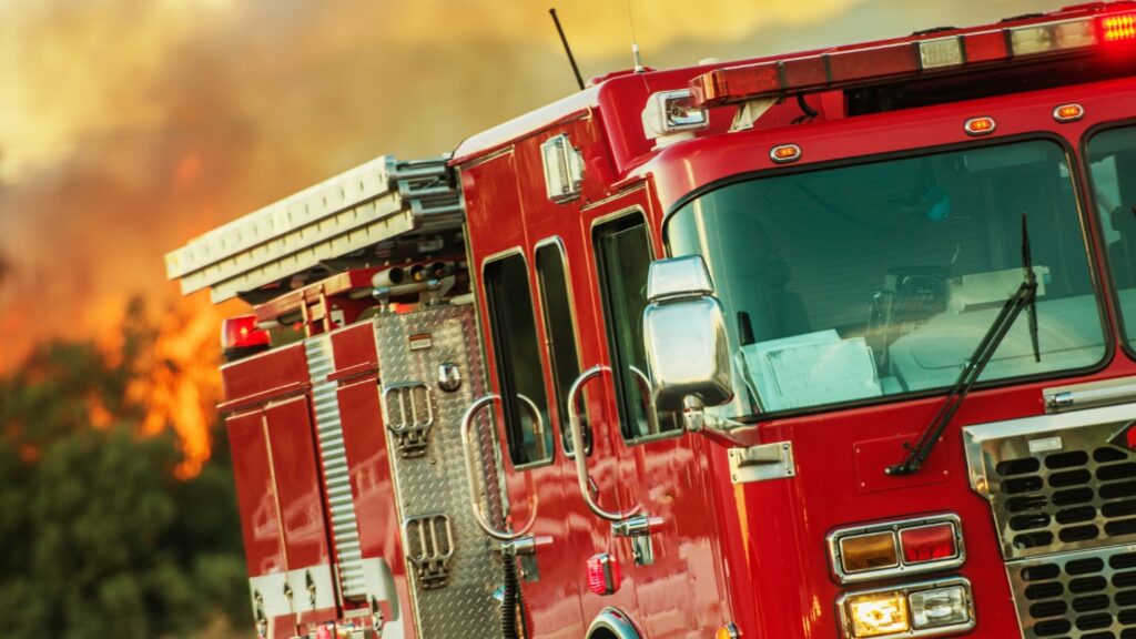 A firetruck with a fire in the back ground burning bright orange.