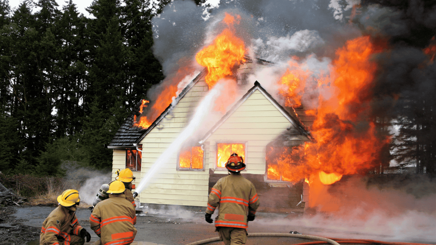 Four firefighters attempt to put out a raging house fire with a fire hose.