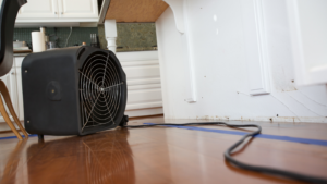 A large fan sits on the floor of a home to dry it after water infiltration.