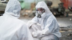 A person in a hazmat suit and mask looks seriously at their work partner.