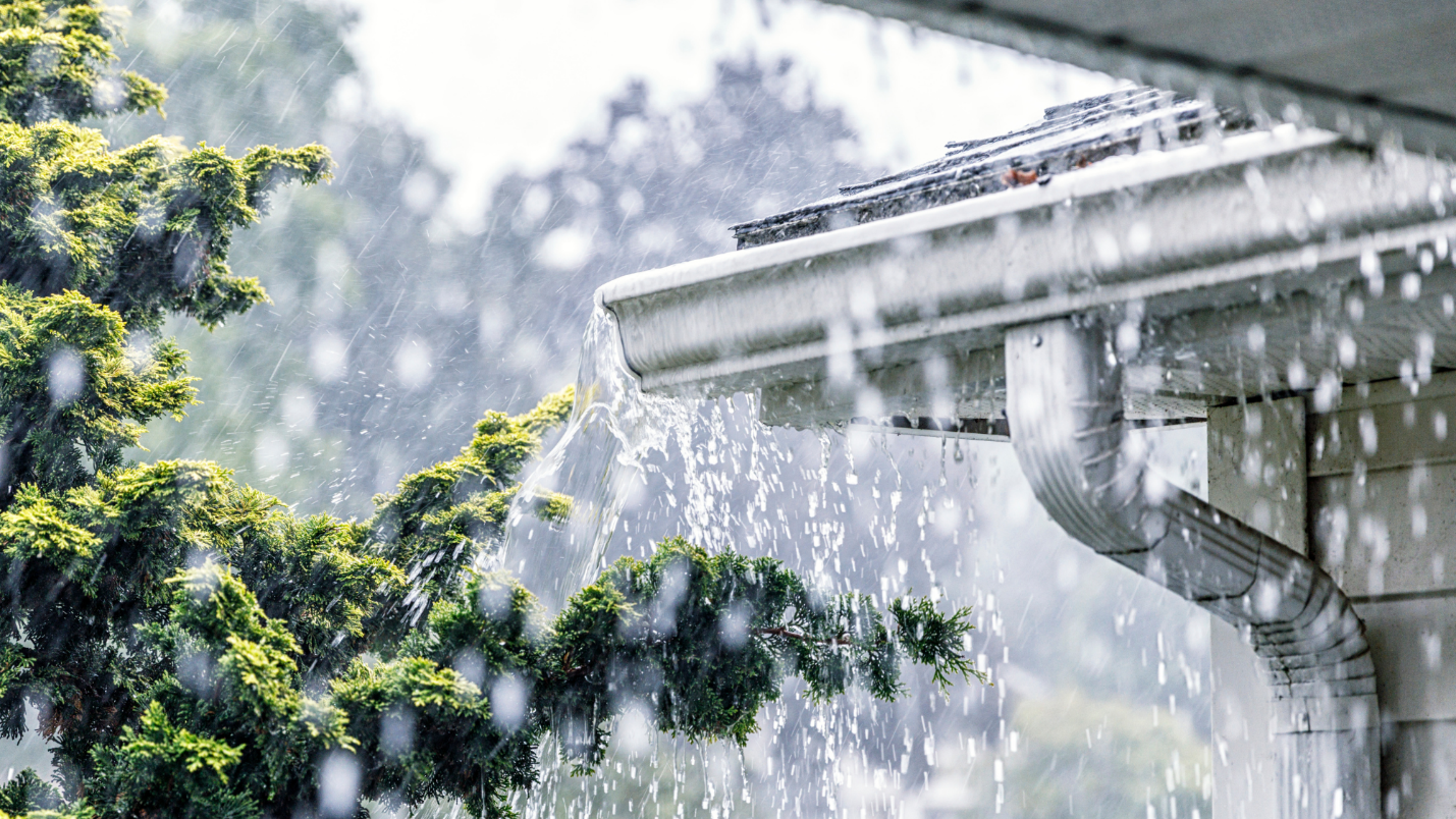 Rain pours down over a home and fills its gutters to overflowing.