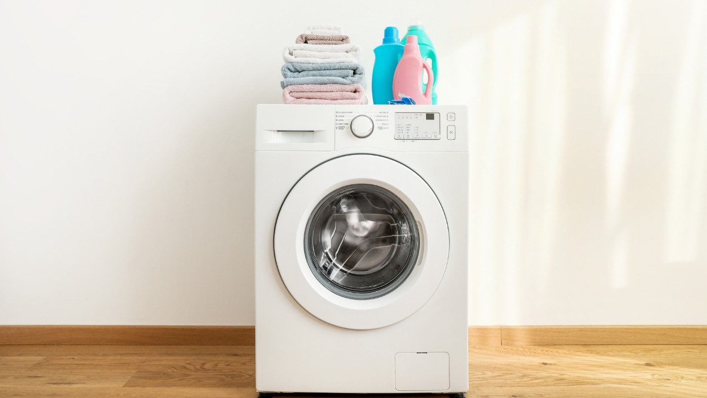 A clean washing machine with folded towels and laundry soap bottles.