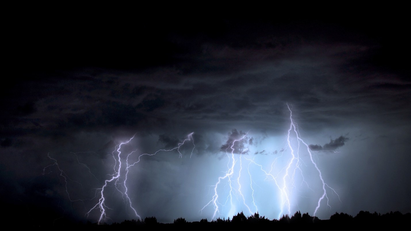 Multiple lighting strikes from a dark grey sky at night.