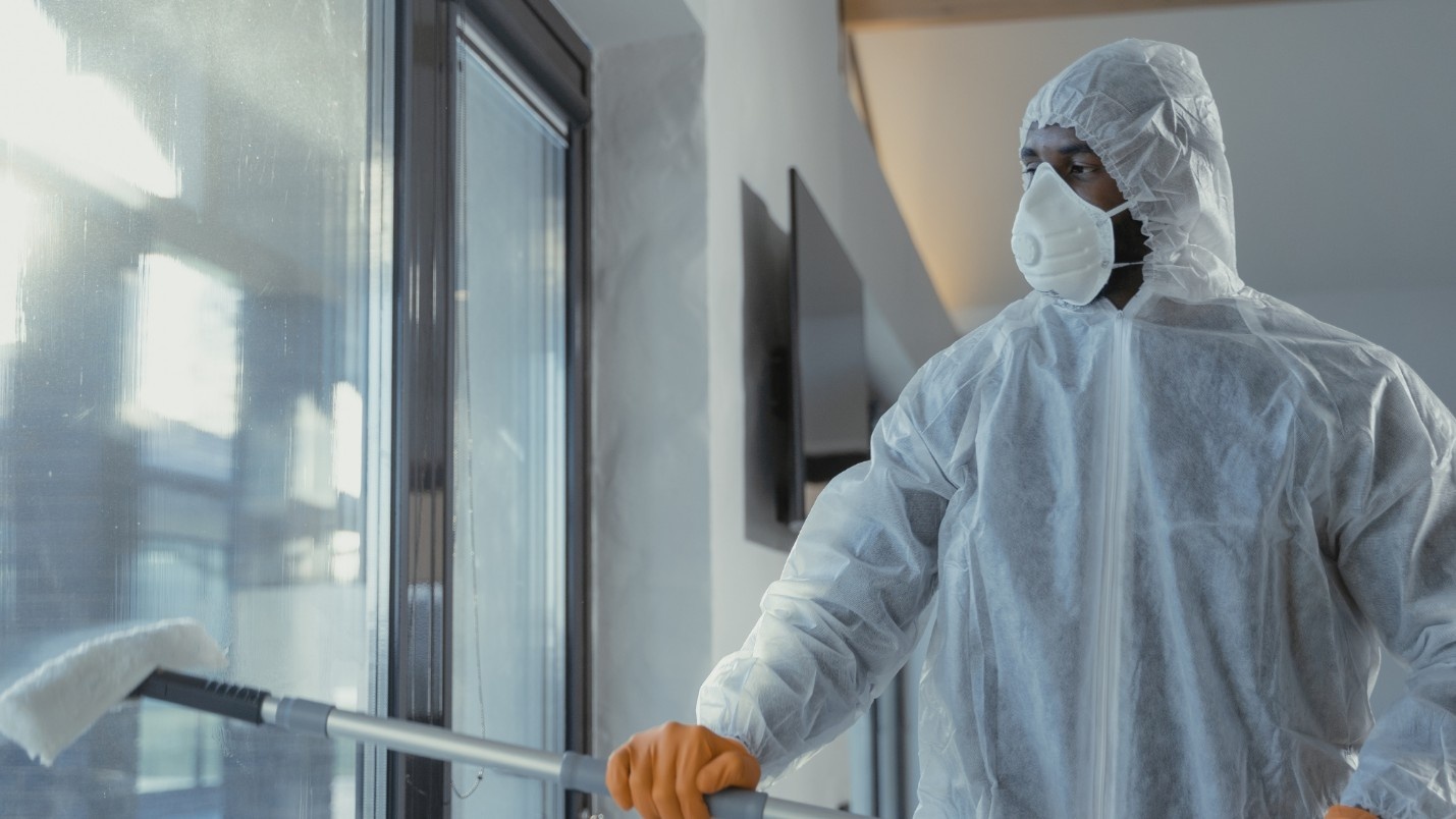 A biohazard technician cleans a glass window with an extended tool.