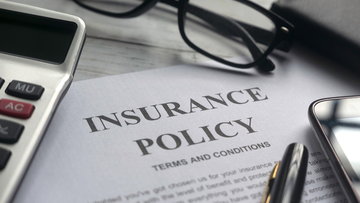 A calculator, pair of glasses and pen surround an insurance policy document.