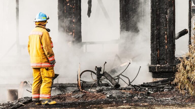 A fireman stands in front of a smoldering home after a house fire.