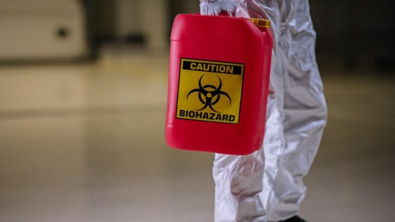 A restoration professional holds a container with a biohazard label on it.