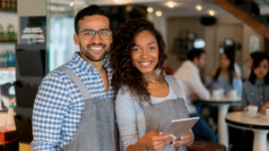 Two small business owners smile in front of their shop.